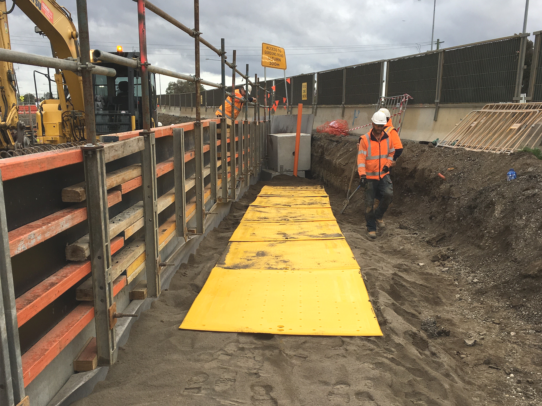 a man in a hard hat walking on a dirt path; overpipe installation